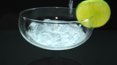 Bir margaritanın makrografisi bir bardağa dolduruluyor canlı bir limon dilimiyle süsleniyor, hepsi siyah arka plana karşı. Her yakın çekim kokteyl ve taze limonun detaylarını yakalar. Geliştirilebilir.