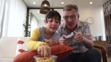 Büyükbaba ve torun birlikte konsol oyunu, eğlence medyası oynuyorlar. Eski kullanım teknolojisi yeni nesil ile iletişim kurar. Nesiller arası uçurum aile bağını güçlendirir. Uyumsuzluk.