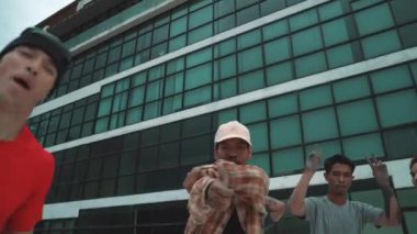 Asyalı profesyonel hippi çatıda arkadaşıyla kameraya bakıyor. Hareket eden kamera, profesyonel break dans takımının şehir ve gökyüzü arka planına sahip kameraya baktığını gösteriyor. Açık hava sporu 2024 hiphop..