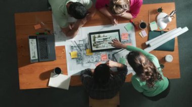 İnşaat mühendislerinin masa başında proje planıyla otururken tablet kullanarak ev yapısını dizayn etmelerine tepeden aşağı bir bakış açısı. Ekip planlama ve inşaat hakkındaki fikirlerin havadan görüşü. Sempozyum.