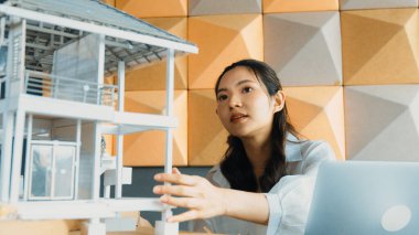 Genç ve güzel mimar mühendisin portresi çatı malzemelerini kontrol ediyor ve ofisteki masaya yerleştirilmiş proje planı ve ev modeliyle dizüstü bilgisayar kullanıyor. Yaratıcı iş tasarımı konsepti. Yönlendirici.