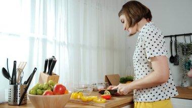 Enerjik anne, mutfak malzemeleri ile çevrili sebzeleri doğrarken modern mutfakta kahvaltı için salata yapıyor. Akıllı kadın temizlikçi yemek pişirir ve yemek hazırlar. Sağlıklı bir yaşam tarzı. Pedagoji.