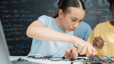 Kafkas öğretmeni STEM teknoloji sınıfında robot araba hazırlarken elektronik alet tamir tahtası kullanan mutlu lise öğrencisi. Tel ve anakart kullanarak çalışan çekici bir kız. Öğretim.