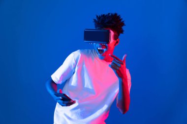 Genç Afrikalı Amerikalı oyuncu sanal gerçeklik dünyasını dijital fütüristik teknolojiye bağlayan mavi neon ışıklı duvarda akıllı telefon oyunu hologramı kullanarak VR kullanıyor. Entrika.