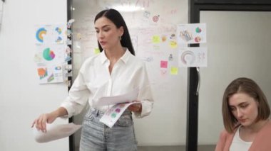 Genç ve güzel iş kadını, iş görüşmesi sırasında cam kurulun önünde zihin haritası olan uzman yatırımcılara toplantı belgeleri ve iş haritası veriyor. Yaratıcı tasarım. Tertemiz..