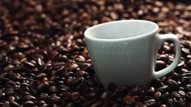 Kahve fincanının içine kahve çekirdeği yığını ile çevrili bir şekilde düşüyor. Beyaz fincana aromatik fasulye döküyorum. Kahvenin üst görüntüsü siyah arka planlı cama düşer. Geliştirilebilir.