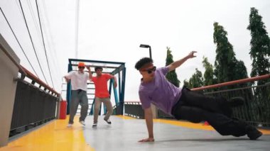 Panorama 'da hipster şık kıyafetler giyer ve dondurucu poz verir. Bir grup profesyonel dansçı break dans yaparken seçkin adam break dans yapıyor. Açık hava sporu 2024. Yumuşak bir şekilde.