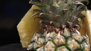 Taze ananaslı ve ayrı siyah arkaplanlı bir ananas dilimli videoyu kapat. Kaba ve balmumu kabuğu, dikenli yeşil yapraklardan bir taç, yemek fotoğrafçılığı. Geliştirilebilir.
