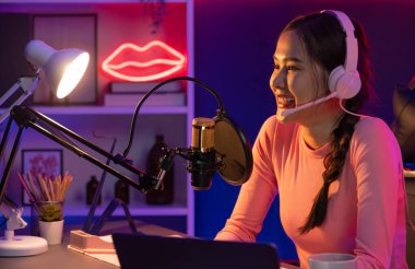 Geceleri podcast 'te olumlu konuşmalar yapan, pembe neon ışıklı modern stüdyoda sunum için dizüstü bilgisayar kullanan, gülümseyen, genç, güzel Asyalı bir etkileyiciydi. Taktik.