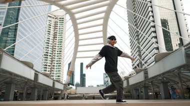 Genç Asyalı hippi şehir merkezinde insanların etrafında ayak izlerini gösteriyor. Şık bir sokak dansçısı B-boy ya da serbest dans eder. Açık hava sporu 2024. Break dans. Yumuşak bir şekilde..