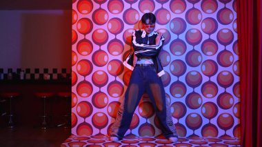 Asyalı break dansçı serbest stile geçiyor ve balon arka planlı kameraya bakıyor. Profesyonel hippi gündelik kıyafet giyer ve gözlük takar. Mutluluk.