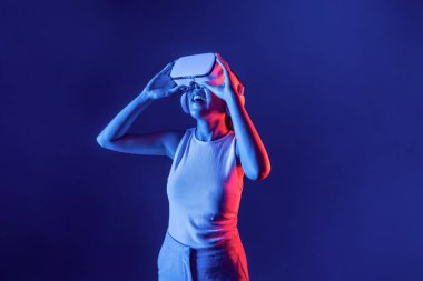 Siberpunk neon ışıklı cihazlarla çevrili zeki bir kadın metaevrene bağlı VR kulaklık takıyor, gelecekçi siber uzay teknolojisi. Zarif bir kadın sanal ortamda yaratılmış gibi görünür. Halüsinasyon.