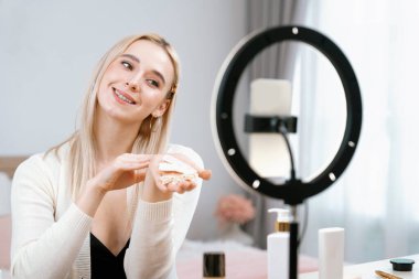 Sosyal medya için güzellik ve kozmetik video içeriği hazırlayan genç bir kadın. Güzellik blogcusu kameraya gülümserken seyirciye ya da takipçilere güzellik teninin nasıl uygulanacağını gösteriyor. Blithe