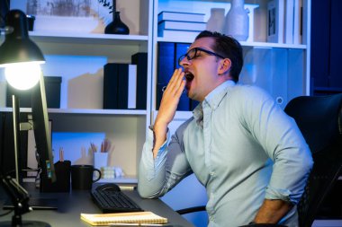 Çalışan bir işadamı, gece vakti projesiyle uykulu bir şekilde e-posta bilgilerinin modern işyerine gönderilmesini bekliyor. Uzaktan kumandalı çevrimiçi çalışmadan zaman içinde sıkılan serbest çalışan teması. Satılabilir.