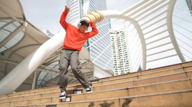 Şehre atlarken kulaklık takan Asyalı hippi. Profesyonel break dansçı şehirde break dans gösterisi yapıyor. Break dans ya da sokak dansı. Açık hava sporu 2024. Yumuşak bir şekilde..