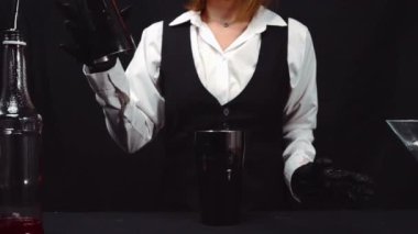 Makrografi, bir barmenin martini bardağına canlı kırmızı bir kokteyl karıştırma sanatına tanık olmak, güzel süslenmiş taze bir biberiye ve parlak siyah bir arka plan. Geliştirilebilir.