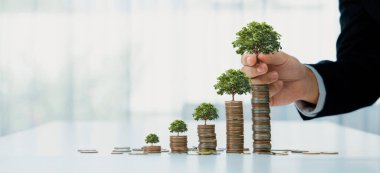 Üzerinde ağaç olan para yığını, CSR ya da ESG 'nin çevreyi koruma amaçlı yeşil iş yatırımlarını sembolize ediyor. Sıfır sürdürülebilirliği arşivlemek için finansal planlama yapan iş adamları. Kurnaz.
