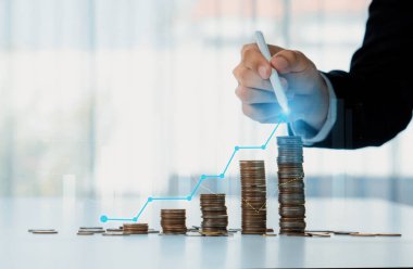 Dijital grafik göstergeli bozuk para yığını iş yatırımını ve ekonomik büyümeyi sembolize ediyor. Finansal hedefe ulaşmak ve kâr sağlamak için finansal planlama yapan bir iş adamı. Kurnaz.