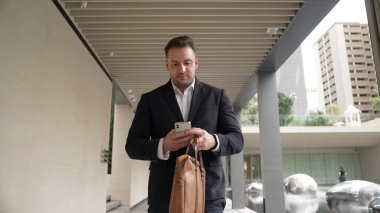 Happy proje yöneticisi koridorda yürürken cep telefonunu kontrol ediyor. Profesyonel iş adamı başarılı projesini kutlarken ya da satışları artırırken takım elbise giyer ve bavulu toplantı için tutar. Urbane.