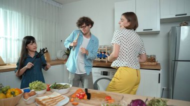 Kafkasyalı anne ukulele çalarken ve mutfakta müzik dinlerken mutlu aile dansları. Asyalı kız mutfakta şarkı söyleyip dans ederken akıllı ebeveynlerle yemek pişirmeye hazırlanıyor. Pedagoji.