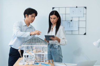 Güzel, genç, beyaz bir proje yöneticisi Asyalı mühendise, mühendislik masasında ev modelini ölçerken tablet kullanarak bina detaylarını anlattı. Tertemiz.