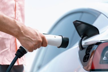 Dışarıdaki şarj istasyonundan EV şarj aletini şarj etmek için elektrikli araca elle tak. Alternatif temiz ve sürdürülebilir enerji kavramına sahip taze gün ışığı ortamı. Kalıcı