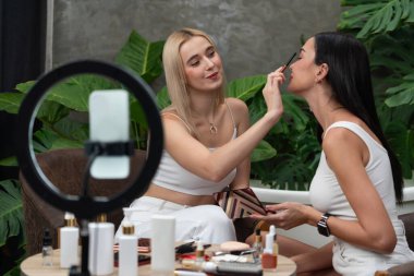 Yeşil bitki bahçesi videosunda doğal güzellik ve kozmetik dersi yapan iki güzel içerik yaratıcısı. Güzellik blogcusu, sosyal medyum izleyicilere güzellik hizmetinin nasıl yapıldığını göstermek için kamera ışığı halkasını kullanıyor. Blithe