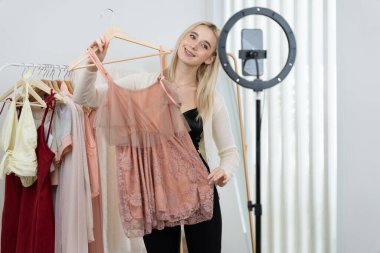 Genç sosyal medyum kadın moda videosu yapıyor. Blogcu kameraya ve ışık çemberine gülümserken, aynı zamanda ikna edici çevrimiçi kıyafetleri izleyicilere veya takipçilere vlog sattırıyor. Blithe