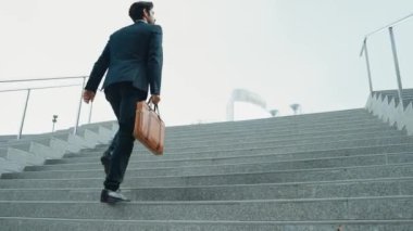 Akıllı bir iş adamının elinde çantayla merdivenlerden yukarı çıkışının en üst görüntüsü. Profesyonel proje yöneticisi merdivenlerden çıkıp işyerine gidiyor. Yeteneklerini arttırmak, terfi almak, seyahat etmek. Sevinçli..