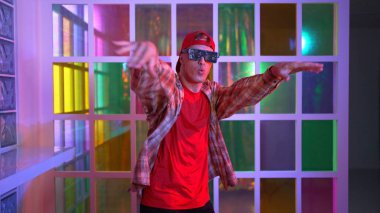 Komik break dansçı kameraya bakarken hiphop 'a doğru serbest adım atıyor. Çılgın mutlu hipster dans edip sokak dansı yaparken Led ışığında günlük kıyafet ve güneş gözlüğü takıyor. Mutluluk.