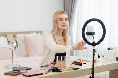 Sosyal medya için güzellik ve kozmetik video içeriği hazırlayan genç bir kadın. Güzellik blogcusu kameraya gülümserken seyircilere ve takipçilere güzellik bakımını gösteriyor. Blithe