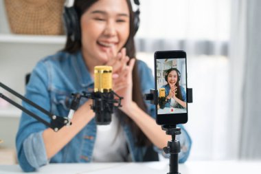 Asyalı sunucu canlı yayında canlı yayında canlı yayında sosyal medyada kulaklık takarak konuşuyor. Dinleyicileri modern stüdyoda koçluk yaparak selamlıyor. Taktik.