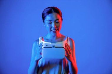 Zeki kadın, neon ışığı altında duran VR kulaklıkla vuruluyor, metaevreni bağlamak için bir cihaz, gelecekteki siber uzay topluluk teknolojisi. Zarif bir kadın, mutlu yüzlü gözlük taşıyıp izler. Halüsinasyon.