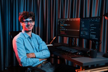 Ekranda yazılım geliştirme bilgisine karşı oturan gülümseyen bilişim geliştiricisinin profili, web sitesindeki son sürüm uygulaması için program kodlaması oluşturarak çevrili kameraya bakıyor. Toplayıcı.