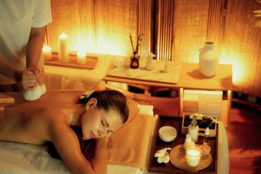 Sıcak bitkisel top spa masaj vücut tedavisi, masör kadın vücuduna nazikçe şifalı bitki torbası bastırıyor. Aromaterapi tesisinin sakinliği ve dinginliği kaplıca salonundaki mumların sıcacık ışığında. Sessiz.