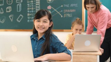 Akıllı Asyalı kız, mühendislik komut yazarken kameraya bakıyor. Çok kültürlü bir öğrenci yapay zekayı öğrenirken öğretmenler sistemi öğretiyor ya da STEM sınıfında sınıfları kontrol ediyor. Pedagoji.