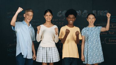 Çeşitli akademik öğrenciler alkışlıyor ve başarılı projeyi el kaldırarak kutluyorlar. Bir grup çok kültürlü çocuk kameraya bakarken elinde mühendislik koduyla tahtada dikiliyorlar. Öğretim.