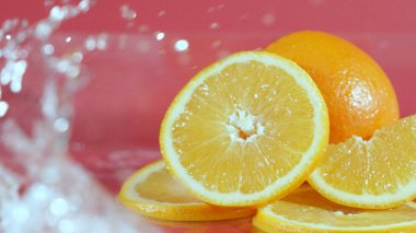 Turuncuyla dilimlenmiş taze portakalı yakın plan kırmızı zemin üzerine su sıçramış. Bir dilim narenciye suyu dökülmüş ve arkaplanda su dalgası olan makrografi. Pabulum.