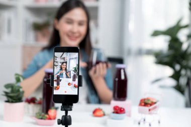 Seçici odaklı akıllı telefon ve gülümseyen genç, güzel Asyalı karışık çilek ve kiraz suyu detoksu değerlendirmesi sosyal medyada sağlıklı ürün tanıtımı sunuyor. Taktik.