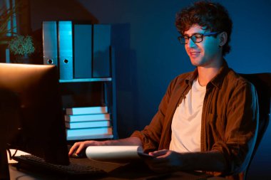 Genç işadamı, Neon Light Modern Ofis 'teki yeni proje surround çalışma masası için kağıt üzerinde tasarım düşünüyor. E-posta ile hediye göndermeden önce not defterine yeni bir iş düşünüyorum. Toplayıcı.