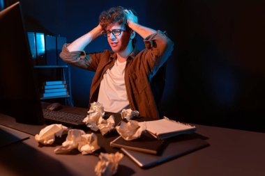 Aşırı çalışan projeyle uğraşan stresli yaratıcı yönetici buruşmuş kağıtların etrafını sararken gece vakti modern ofisteki gündelik gömlekle dizüstü bilgisayar ekranına e-posta göndermeyi bekliyor. Toplayıcı.