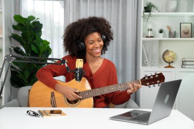 Genç Afrikalı Amerikalı müzisyenin sunucu kanalı gitar çalıyor, şarkı söylüyor, stüdyoda dizüstü bilgisayardan yayın yapıyor. Kulaklık dekorasyonu ve mikrofon kaydı. Tatlandırıcı.