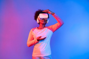 Genç Afrikalı, metaevren üzerinden VR gözlük takıyor ve elinde mavi pembe neon ışık grafikli dijital yenilik üzerine veri öğrenme uygulaması tutuyor. Entrika.