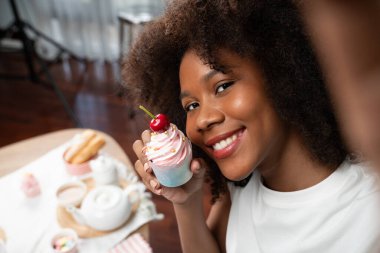 Genç ve güzel Afrikalı blogcu akıllı telefondaki selfie ile konsept özel mutfak konseptinde kek sunuyor. Favori tatlı fırın yemeğiyle sosyal medyanın yaratılması. Tatlandırıcı.