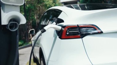 Yavaş çekim EV elektrikli araba yazın yeşil sürdürülebilir şehir bahçesinde şarj oluyor. Kentsel sürdürülebilirlik yaşam tarzı yeşil temiz yeniden şarj edilebilir enerji elektrikli BEV araç iç organları