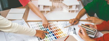 Yetenekli mimar takımı ev inşaatı hakkında tartışırken, iç mimar ev modeli ve bina planının dağıldığı renk paletine uygun bir renk belirliyor. Üst Manzara. Değiştirilmiş.