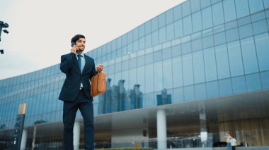 Akıllı iş adamı binada yürürken telefonla konuşuyor. İş planı, pazarlama stratejisi ya da çalışma hakkında konuşmak için akıllı telefonla konuşurken sokakta yürüyen mutlu bir yönetici. Sevinçli..