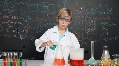 Akıllı çocuk, laboratuvar şişelerinde karışık kimyasal sıvıları dikkatlice inceler. Beyaz çocuk kimya dersi ya da BTMM fen dersinde bir deney yapmaya odaklan. Etkinlik.