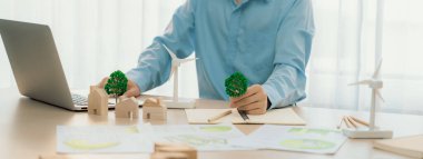 Profesyonel mimar bir eko evde yeşil tasarım kullanmayı planlıyor. Yetenekli bir mühendis, ev ve yel değirmeni modelinin etrafa saçıldığı bir masada dizüstü bilgisayar kullanarak bir ekolojik ev planı tasarladı. Tanımlama.