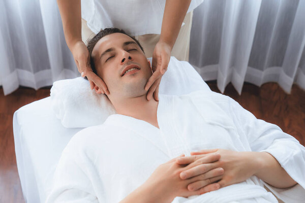 Кавказский мужчина наслаждается расслабляющим анти-стрессовым массажем головы и расслабляющим отдыхом кожи лица в дневном спа современном светлом окружении на роскошном курорте или в спа-салоне отеля. Quiescent